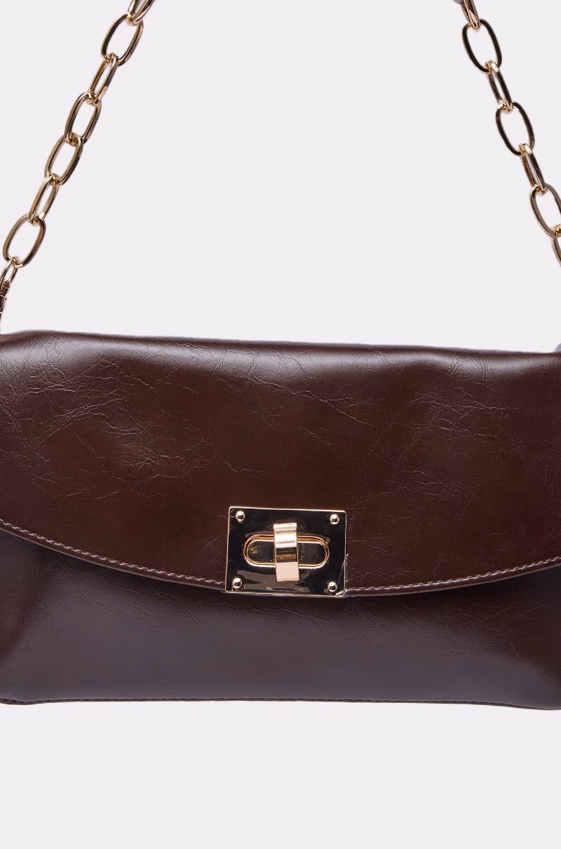 The BUTTER SOFT PURSE is a dark brown bag featuring a gold turn-lock clasp and gold chain strap, displayed against a plain white background. 3
