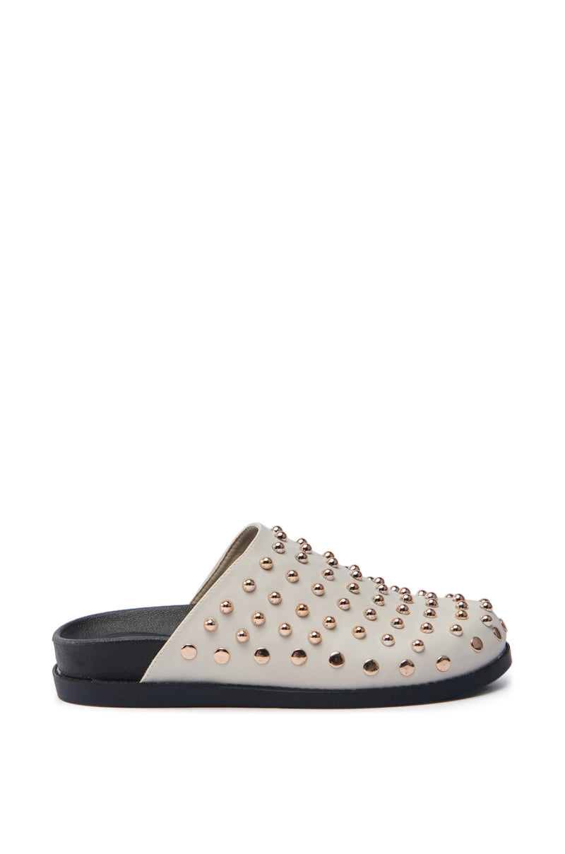 The AZALEA WANG TRAVERSE BEIGE CLOG showcases a slip-on design with a white vegan leather upper, gold metallic stud embellishments, a black sole, and a flat heel as seen from the side.