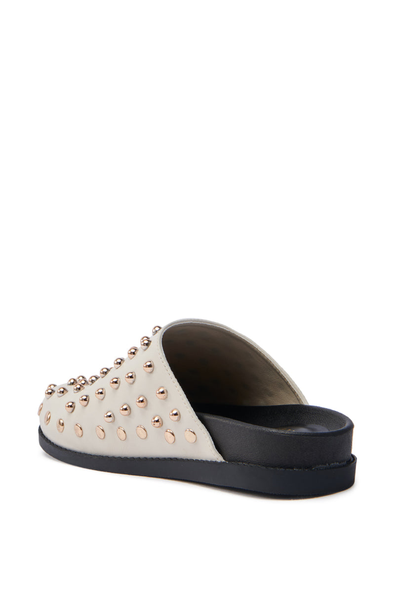 The AZALEA WANG TRAVERSE BEIGE CLOG is a stylish, sustainable slip-on shoe made from vegan leather featuring a cream upper with gold metallic studs. It includes an angled open back and a black sole.