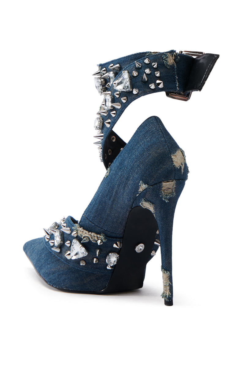 The AZALEA WANG TRIANA DENIM EMBELLISHED PUMP is a high-heeled pump crafted from distressed denim fabric, featuring a pointed toe, thin stiletto heel, ankle strap, and adorned with metal spikes and rhinestones for an edgy design. 5