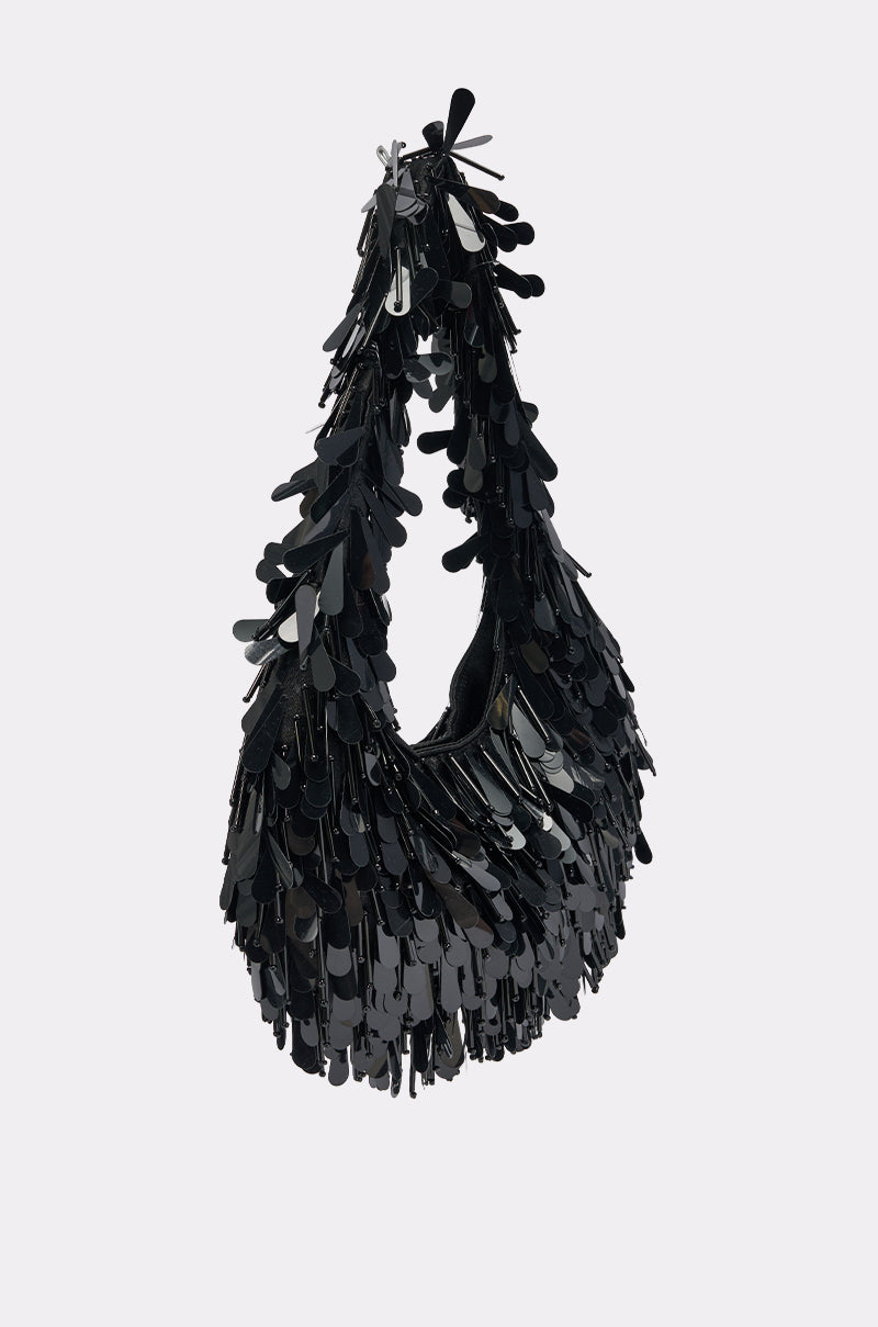 THE NOSTALGIA SEQUIN PURSE IN BLACK is a crescent-shaped hobo bag, covered in shiny, overlapping sequins for a textured, reflective effect—shown against a plain light background.