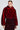 Dressed in the opulent NOW YOU SEE ME FAUX FUR BOMBER IN RED by AKIRA Label, paired with a dazzling red and black skirt, they present an elegant image. Their hair is impeccably styled, and they wear drop earrings while posing against a neutral backdrop.