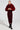 A person confidently stands wearing the NOW YOU SEE ME FAUX FUR BOMBER IN RED over a red sequined dress. They have sleek hair and complement their look with black high-heeled boots, set against a plain white background.