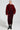 A woman strikes a pose in a stylish outfit, showcasing the AKIRA Label NOW YOU SEE ME FAUX FUR BOMBER IN RED layered over a textured, ruched red dress. She completes her look with black high-heeled boots and oversized hoop earrings, all against a minimalist backdrop.