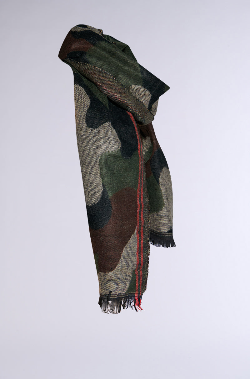 Presenting the Camo Nights Scarf: an oversized design showcasing cozy knit craftsmanship. Set against a neutral background, its camouflage pattern in green, brown, and beige is highlighted by fringed ends and a bold red stripe along one edge.