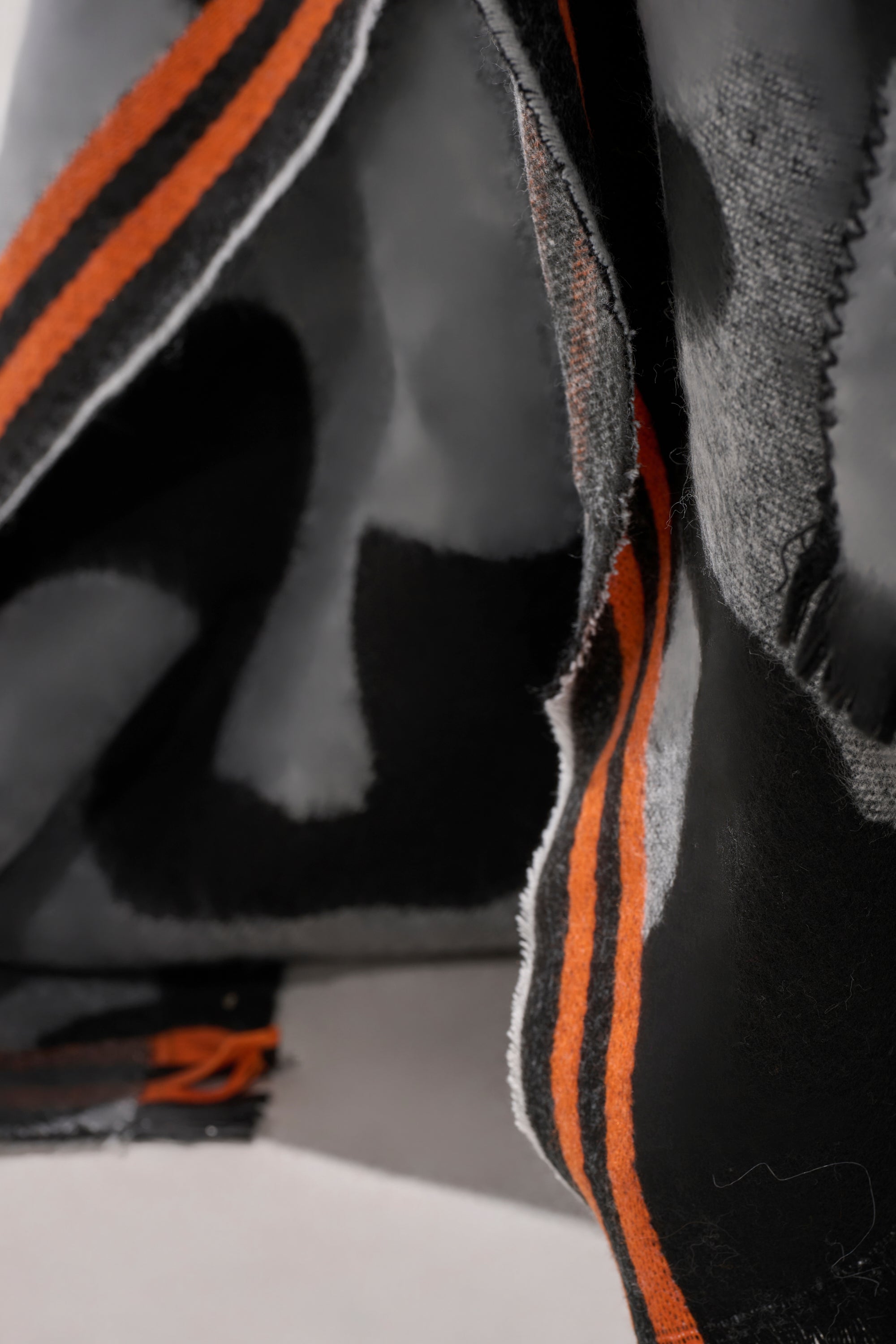 Close-up of the MOD LIFE CAMO PONCHO, showcasing soft black and gray fabric with frayed edges and two bright orange border stripes—a cozy, textured layer for any Mod Life style.