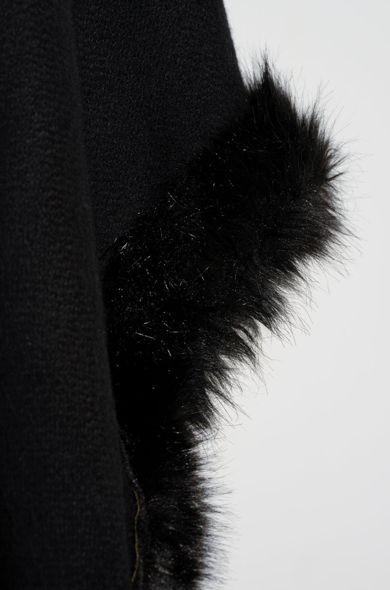 Close-up of the LOVE MY LIFE FAUX FUR TRIM PONCHO in black fabric, highlighting the texture and contrast between its smooth material and fluffy faux fur edge. Set against a soft gray background, it emphasizes the winter-ready details and oversized silhouette.