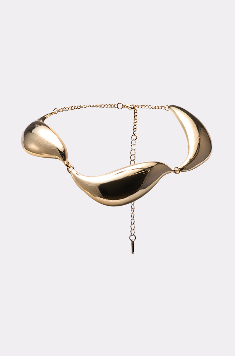 The SUSU NECKLACE is a gold-tone statement collar featuring three large, curved polished metal segments connected by small rings and an adjustable chain clasp. Displayed on a light gray background. 0