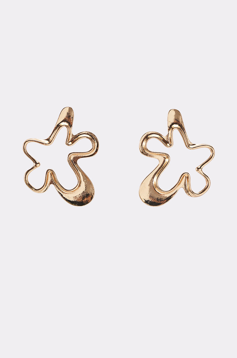 The VIC EARRING is a pair of gold-tone statement earrings featuring abstract, irregular flower shapes with smooth, flowing edges, shown on a plain white background. 1
