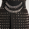 A close-up of a person wearing a black studded jacket with silver spikes, cinched at the waist with THE REGAL CHAIN BELT—a wide black elastic belt adorned with two hanging faux silver metallic Cuban chain links.