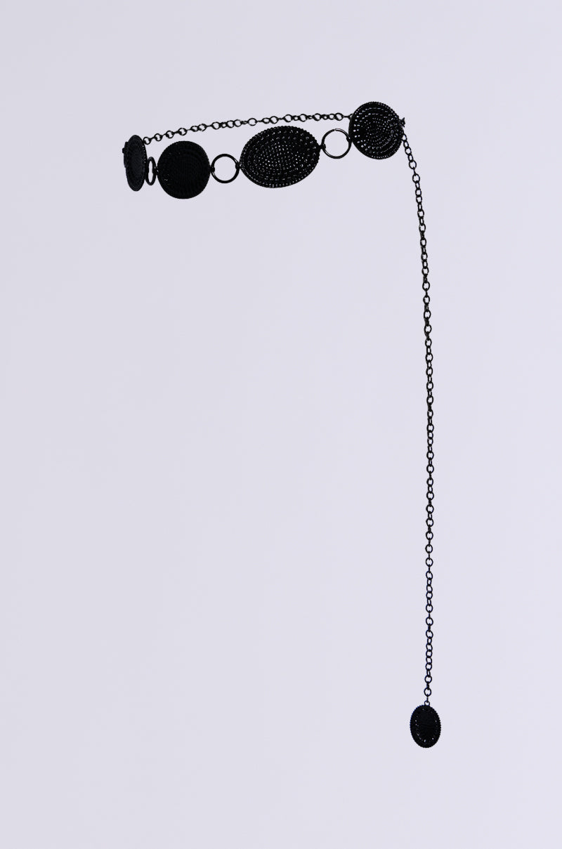 The CARTER BLING CHAIN BELT is a stylish black accessory adorned with asymmetrically arranged oval and round pendants. It features a long chain extension decorated with rhinestone details at the end, all set against a plain light gray background. 5