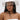 A woman wears the TEST MY LUCK HORSESHOE HAT, a white Western hat adorned with a horseshoe emblem and rhinestone fringe, secured under her chin. She pairs it with a white textured strapless top with metallic accents.