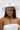 A woman wears the TEST MY LUCK HORSESHOE HAT, a white Western hat adorned with a horseshoe emblem and rhinestone fringe, secured under her chin. She pairs it with a white textured strapless top with metallic accents.