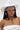 A woman wears the TEST MY LUCK HORSESHOE HAT—a white Western hat with a silver horseshoe, rhinestone fringe, and chin strap. She has long dark hair, pink eyeshadow, and a white strapless top.
