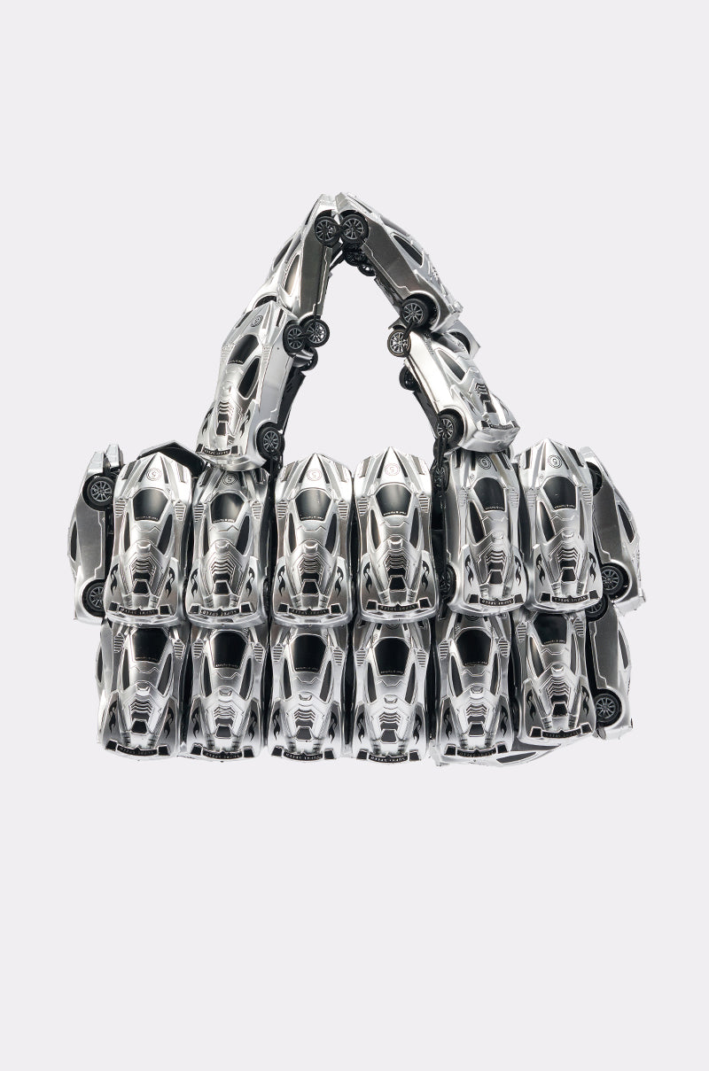 The VROOM VROOM CAR PURSE is a statement handbag made from silver toy sports cars, arranged in rows for the bag's body and handle, with a striking chrome finish set against a plain light background. 1