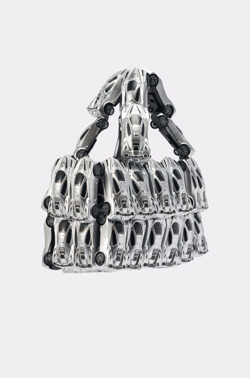 The VROOM VROOM CAR PURSE is a sculptural handbag made from rows of silver toy sports cars, including handles crafted from toy cars, shown against a plain light background. 3