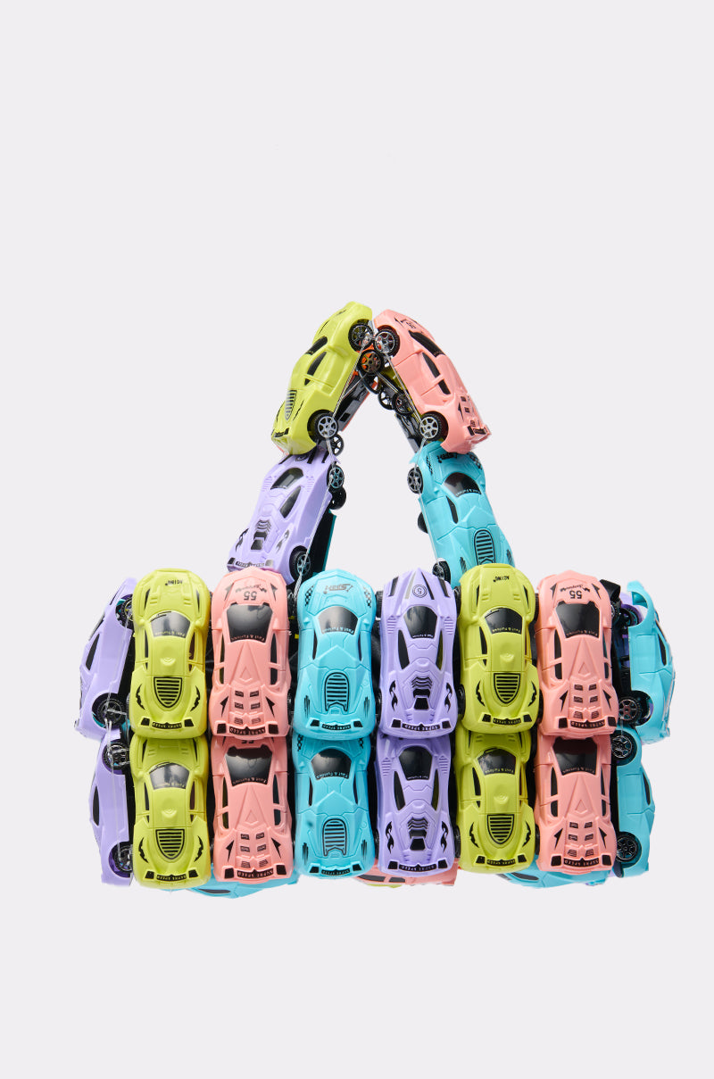 The VROOM CAR PURSE is a novelty handbag sculpture featuring rows of candy-colored toy cars in pink, purple, blue, and yellow, artfully stacked and arranged against a plain white background.