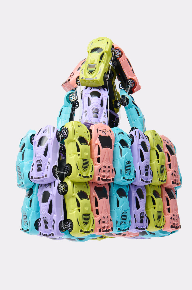 A pyramid of toy cars in green, pink, blue, and purple stacked on a white background, evoking the playful look of the VROOM CAR PURSE—a novelty handbag inspired by candy-colored car designs.