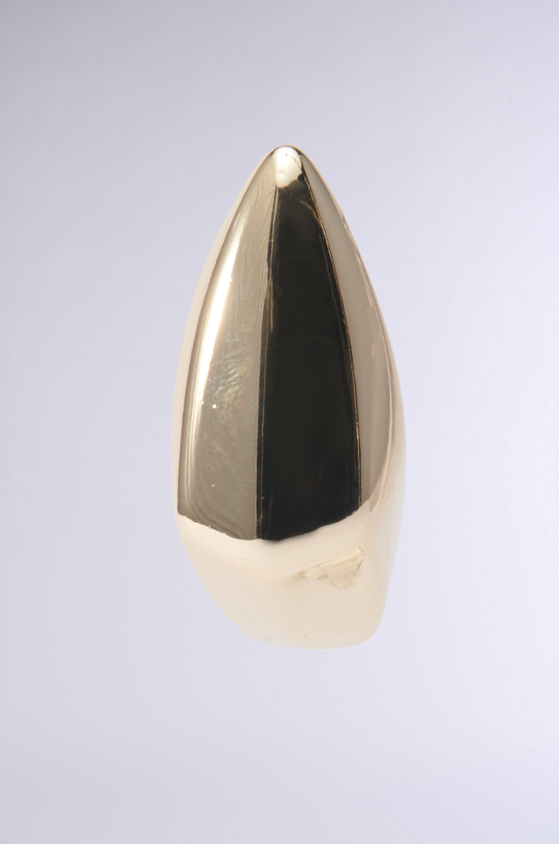 A smooth, elongated sculpture with a reflective faux gold surface is suspended against a plain white background. This sculptural form resembles the sleek, pointed ZELLY STATEMENT EARRING, capturing the spirit of modern abstract art. 3