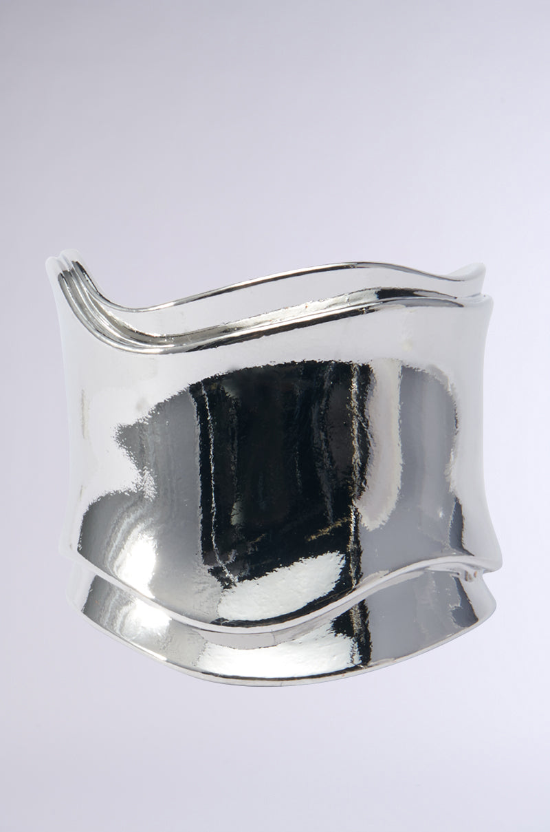 The Sisi Statement Bracelet Cuff in Silver is a chic piece showcasing smooth, flowing curves and a polished faux silver metallic finish against a light gray background. 0
