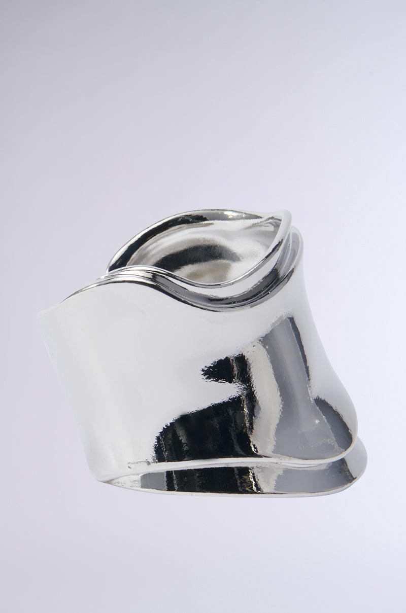 The SISI STATEMENT BRACELET CUFF IN SILVER, with its sleek and flowing curves and a faux silver metallic finish, resembles an organic, chic piece of jewelry set against a plain gray background. 2