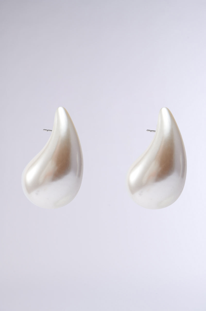 The PEARLESCENT VIBES STATEMENT EARRING showcases a lustrous, abstract teardrop design on a neutral grey backdrop, reflecting light elegantly.