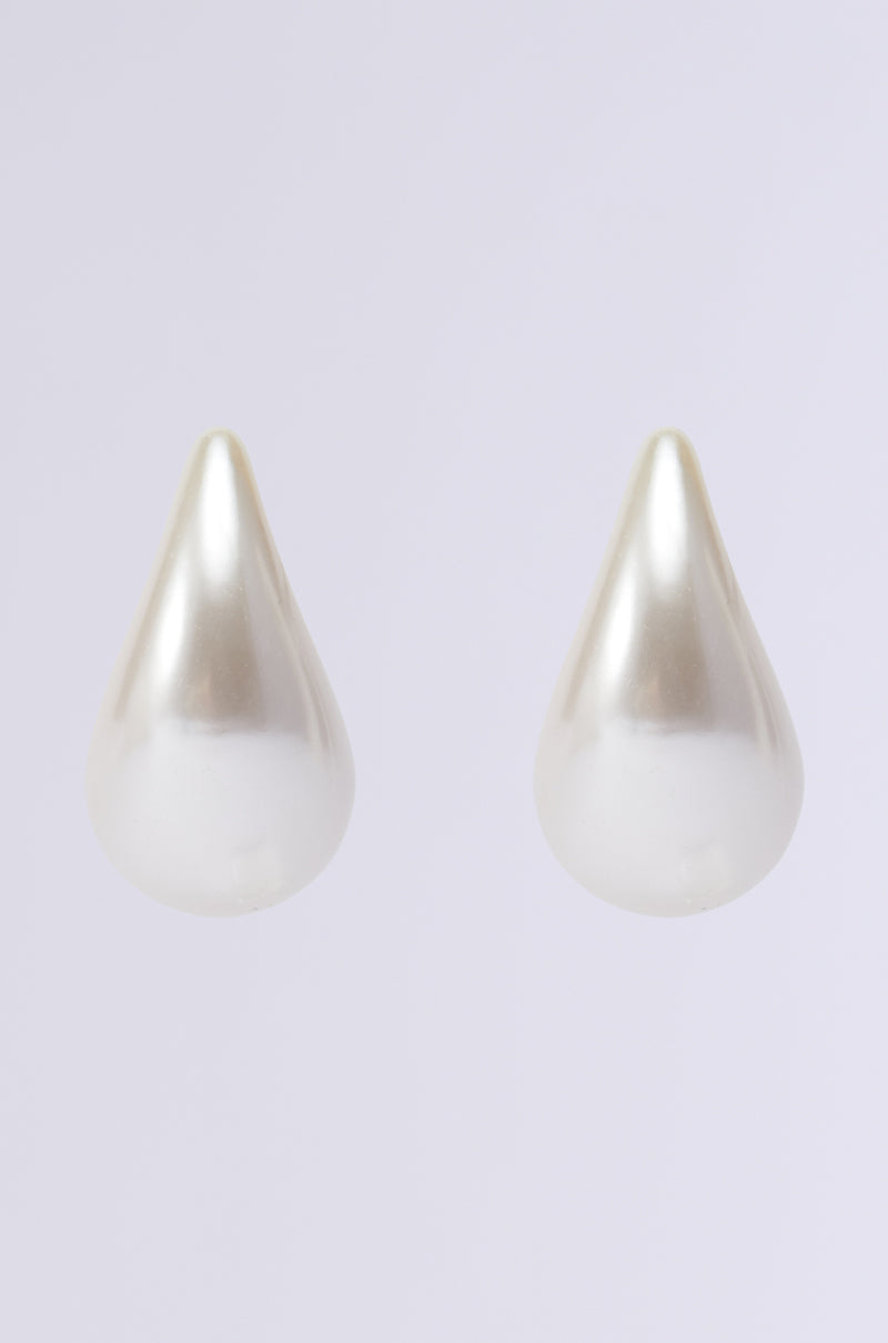The PEARLESCENT VIBES STATEMENT EARRING, featuring two teardrop-shaped pearls, stands out against a plain gray background with its smooth and shiny surface that elegantly reflects light. 3