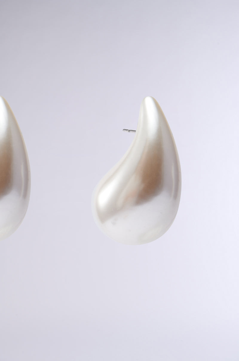 Close-up of the shiny PEARLESCENT VIBES STATEMENT EARRING, showcasing its teardrop silhouette on a plain light background. Half of the pair is visible, emphasizing its distinct shape and glossy finish. 4