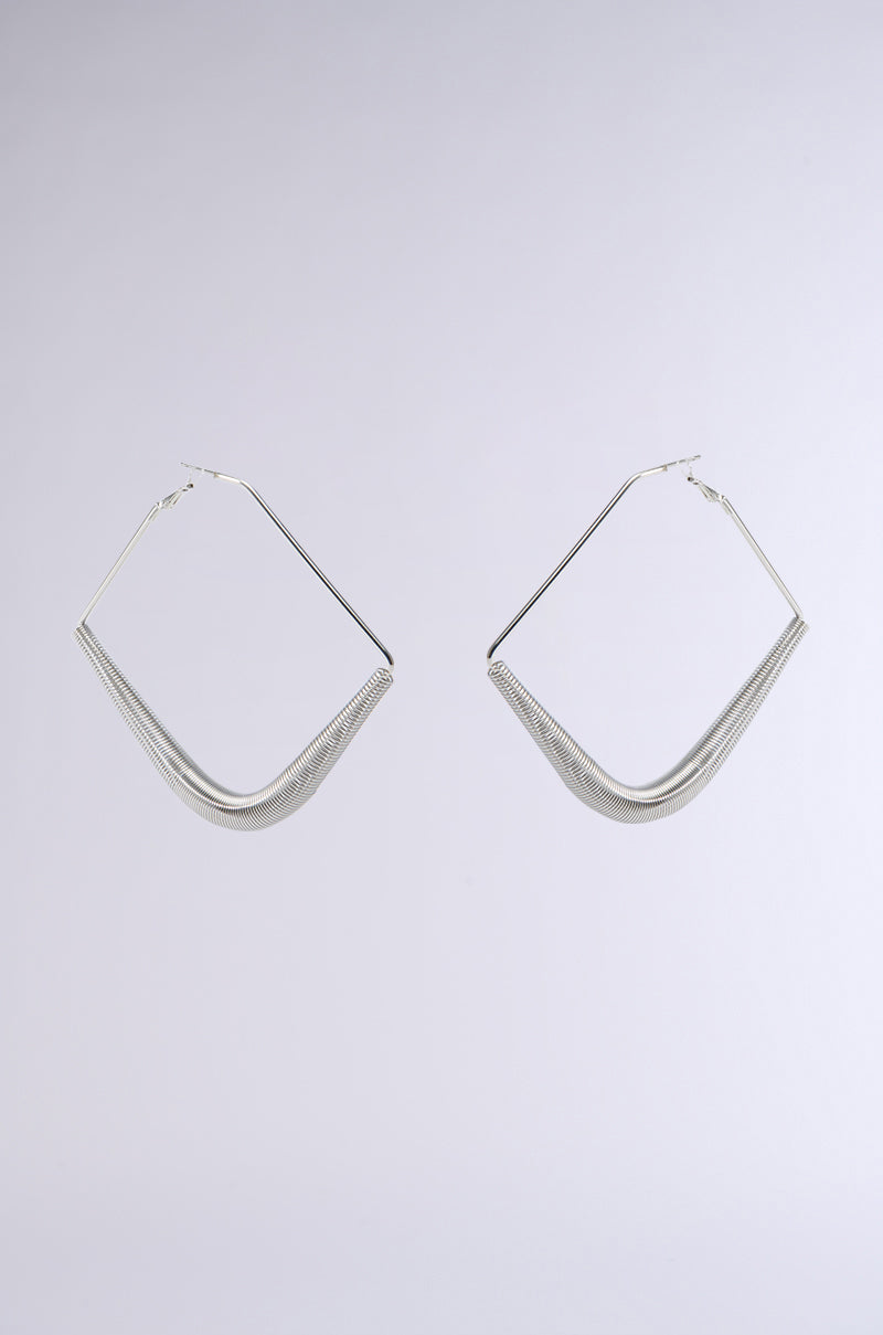 Introducing "THE BIGGER THE HOOP EARRING," a pair of silver geometric earrings with a modern design. These earrings feature a distinctive curved triangular shape, accented by subtle coil spring detailing, and boast a sleek and shiny finish. Displayed against a neutral light background, they capture attention with their stylish allure.