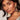 A woman with long dark hair and smooth skin wears a white top and the YOUR MAJESTY EARRING, a large cross-shaped earring embellished with rhinestones and colorful gemstones, gazing into the camera with confidence.