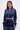 A woman wears the CALL BACK SATIN BOMBER, a shiny navy blue cropped jacket with pearl and rhinestone trim, paired with matching high-waisted pants. She has long straight hair, statement earrings, and a neutral expression.