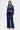 A woman faces forward in the CALL BACK SATIN BOMBER, a navy blue cropped zip-up jacket with wide-leg pants, featuring decorative white bead detailing along the jacket shoulders and pant upper edge.