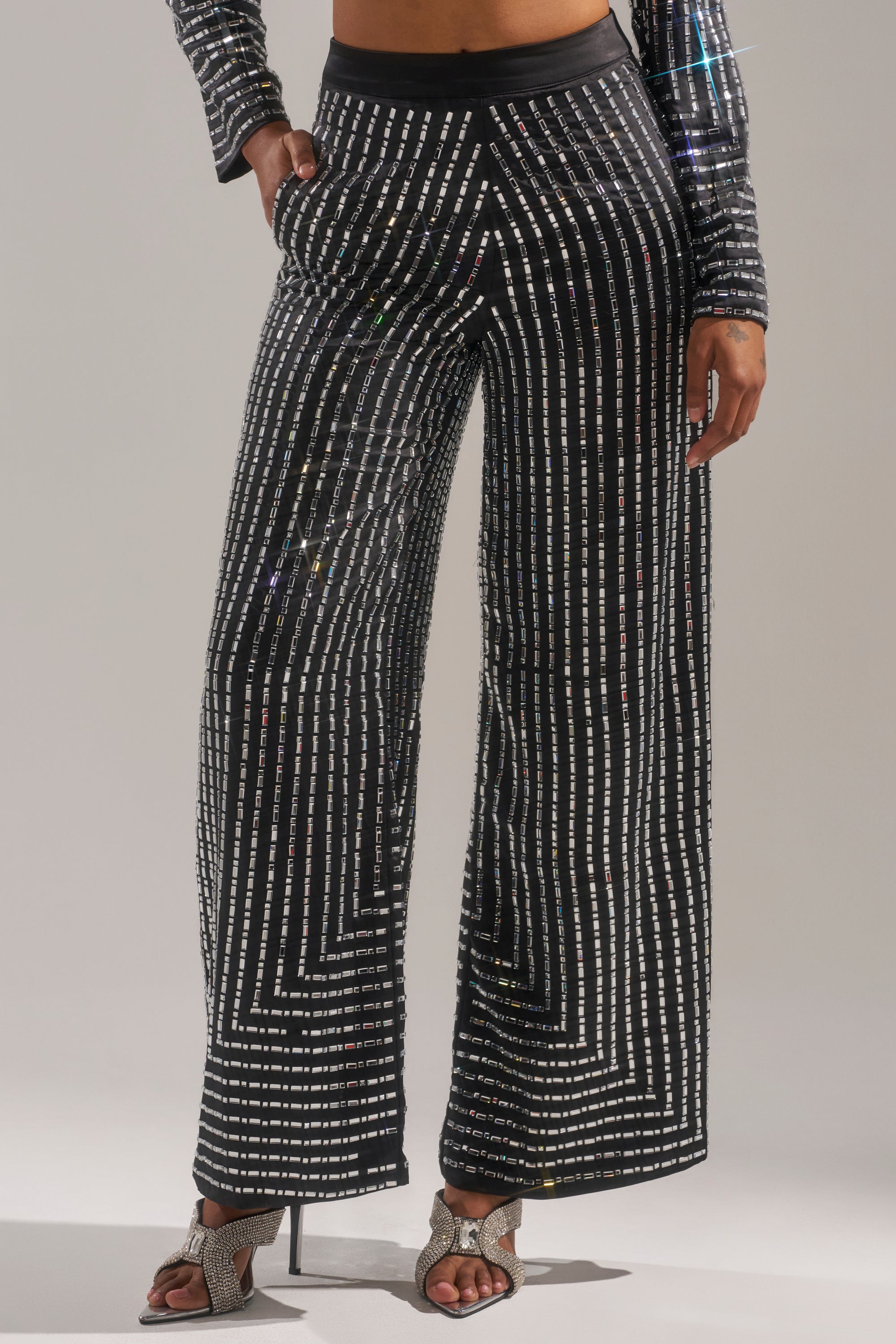Wearing the DONT STARE TOO HARD RHINESTONE TROUSER—wide-leg, black, high-rise pants with sparkling silver stripes—paired with heeled sandals and a coordinating long-sleeve top.