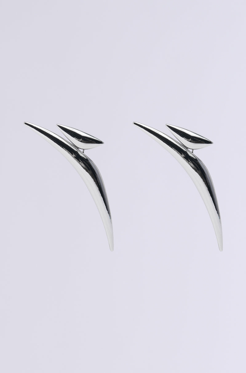 Introducing the KEL EARRING: a pair of sleek, oversized earrings featuring an abstract-shaped, curved design with a metallic faux silver finish, set against a plain white background.