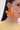 Close-up of a woman with straight brown hair tucked behind her ear, wearing the FRESH START FLOWER EARRING—a large orange acrylic piece—paired with a light yellow pleated sheer top, making it a perfect spring-style accessory.