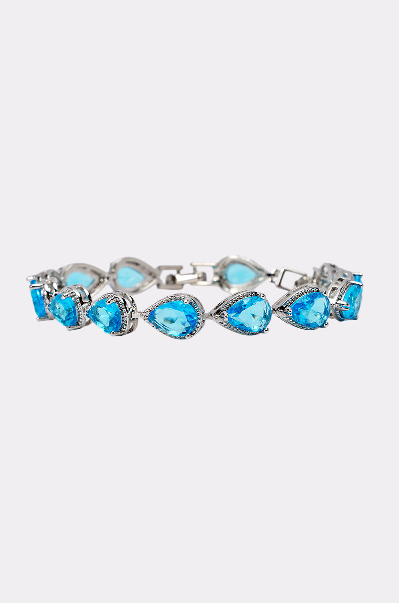 The AQUA CZ BRACELET showcases pear-shaped blue gemstones set in individual links, each outlined by sparkling clear cubic zirconia stones, and is elegantly displayed on a plain white background—a stunning choice for wedding guest jewelry.