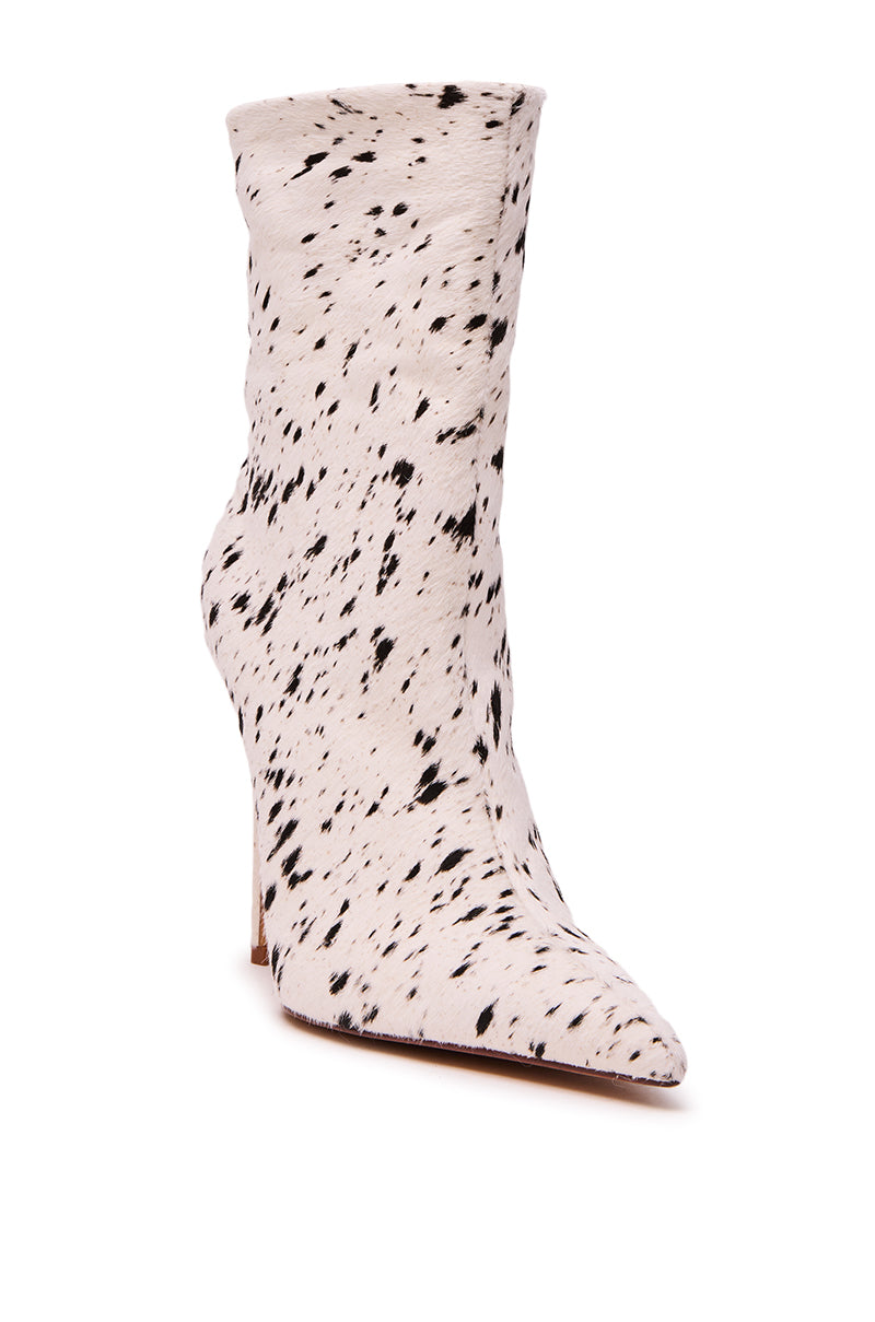 The AZALEA WANG TYELOR WHITE BLACK PONY HAIR BOOTIE is a mid-calf, pointed-toe stiletto bootie with white faux fur and black cow-print spots.