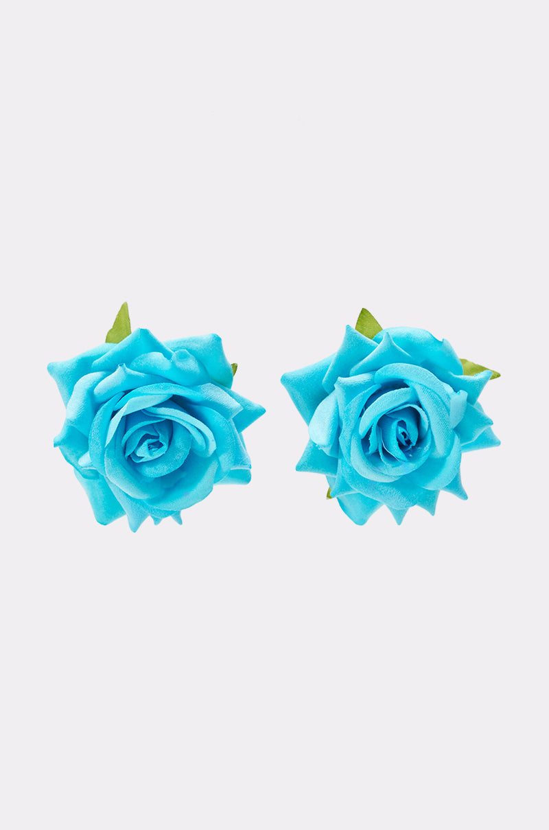 The IN BLOOM EARRING features two vibrant blue artificial rose flowers with green leaves, side by side on a white background, capturing the playful charm of boho-chic summer accessories.