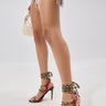 A person in frayed denim shorts and AZALEA WANG TZILLA MULTI COLOR ROPE STILETTO SANDALS holds a small white woven handbag while standing against a plain, light background.