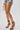 A person in distressed denim shorts and holding a white woven handbag models the AZALEA WANG TZILLA MULTI COLOR ROPE STILETTO SANDAL against a plain light background.
