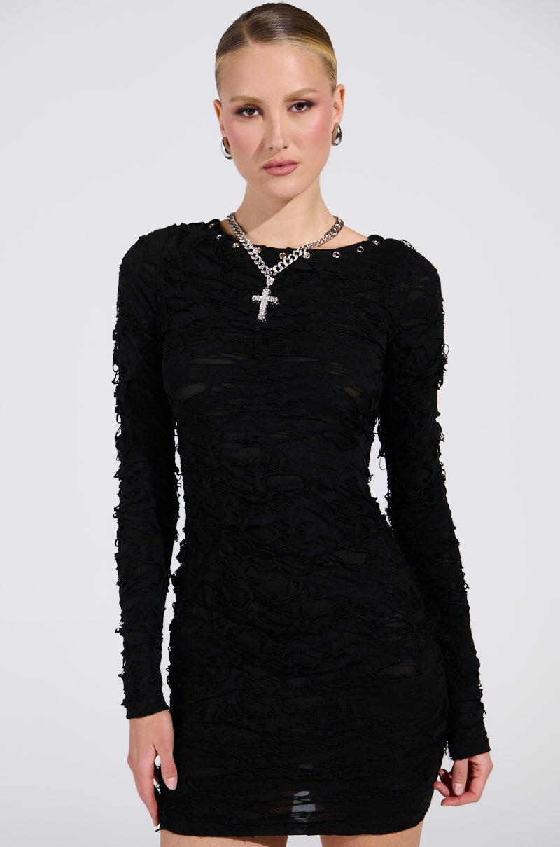 With short, slicked-back hair, a person exudes elegance in the curve-hugging LOTS OF LOVE LACE MINI DRESS. The look is completed with a cross necklace against a plain white background.