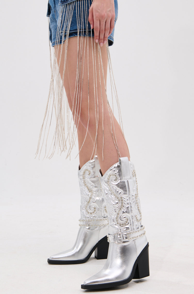 A person wears the AZALEA WANG UMBRA SILVER WESTERN BOOT with baroque embroidery, denim shorts, and long silver beaded fringe, standing on a light-colored floor against a plain white background.