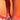 A person stands on a red-lit surface wearing AZALEA WANG UMBRIA SILVER PVC FLOWER WEDGE SANDALS with sculpted heels and tulle pom-poms, showing only their lower legs and feet.