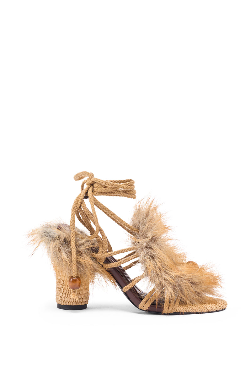 The AKIRA GOLD UMIKA BROWN FUR CHUNKY SANDAL features a woven straw platform, fluffy tan and beige fur accents, strappy leather details, and a wrap-around ankle tie with wooden bead decorations.
