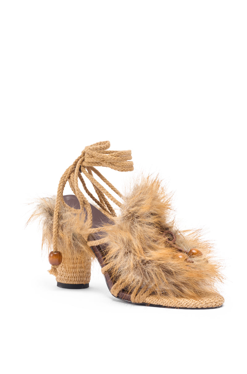 The AKIRA GOLD UMIKA BROWN FUR CHUNKY SANDAL features a woven rope heel, tan faux fur straps with ankle wrap ties, and decorative beads, shown against a white background.