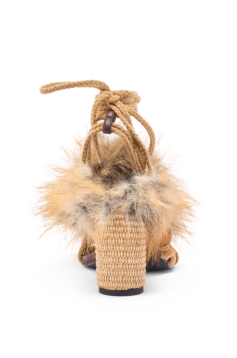 The AKIRA GOLD UMIKA BROWN FUR CHUNKY SANDAL showcases a back view with woven straw material, a block heel, tan fur trim, and rope-style ankle straps against a white background.