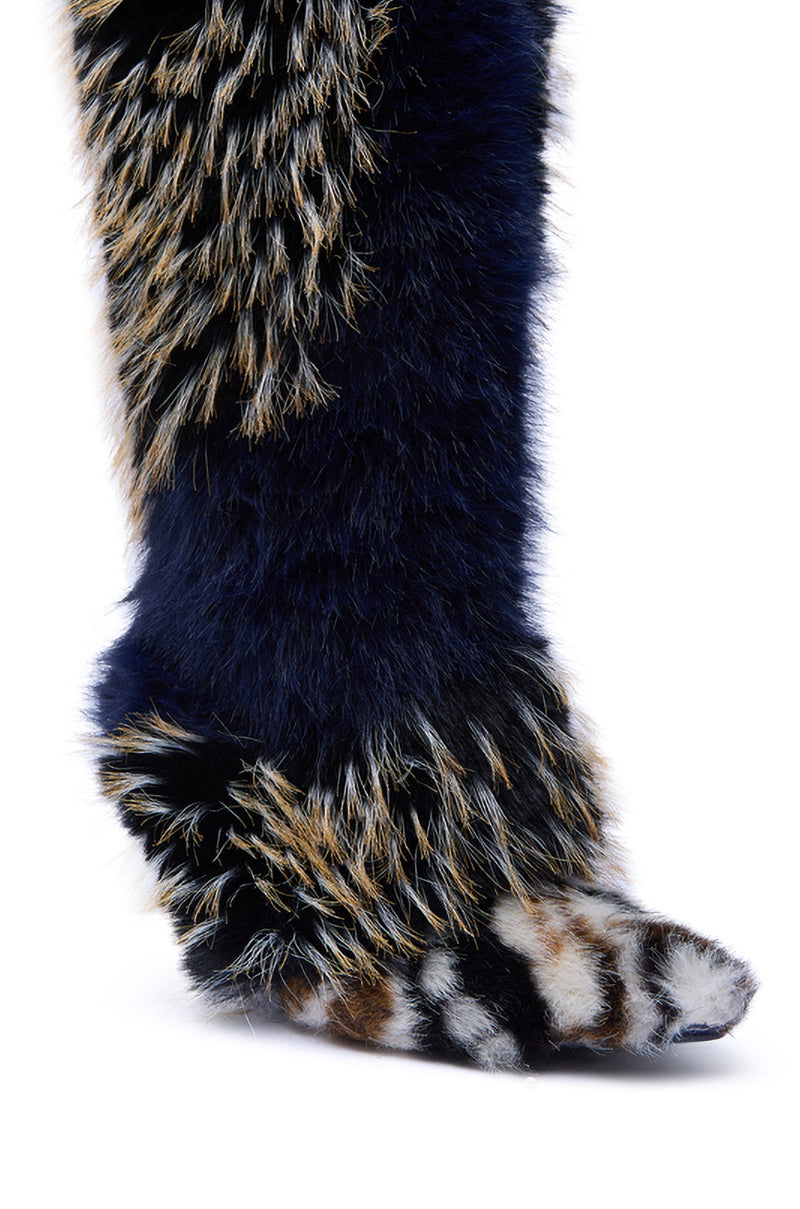 A close-up of a leg and foot wearing the AZALEA WANG UPENDO NAVY MULTI FUR BOOT, featuring plush, dark blue speckled faux fur and a paw-inspired shape for a bold, animal-inspired look.