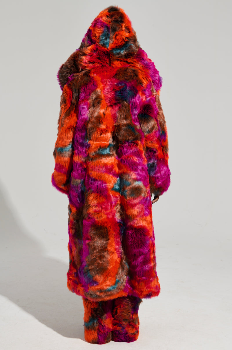 Wearing an eye-catching, oversized pink multi-colored faux fur coat called the "UPSETTER MAXI," a person stands with their back to the camera. The look is completed with matching faux fur pants against a plain gray background.