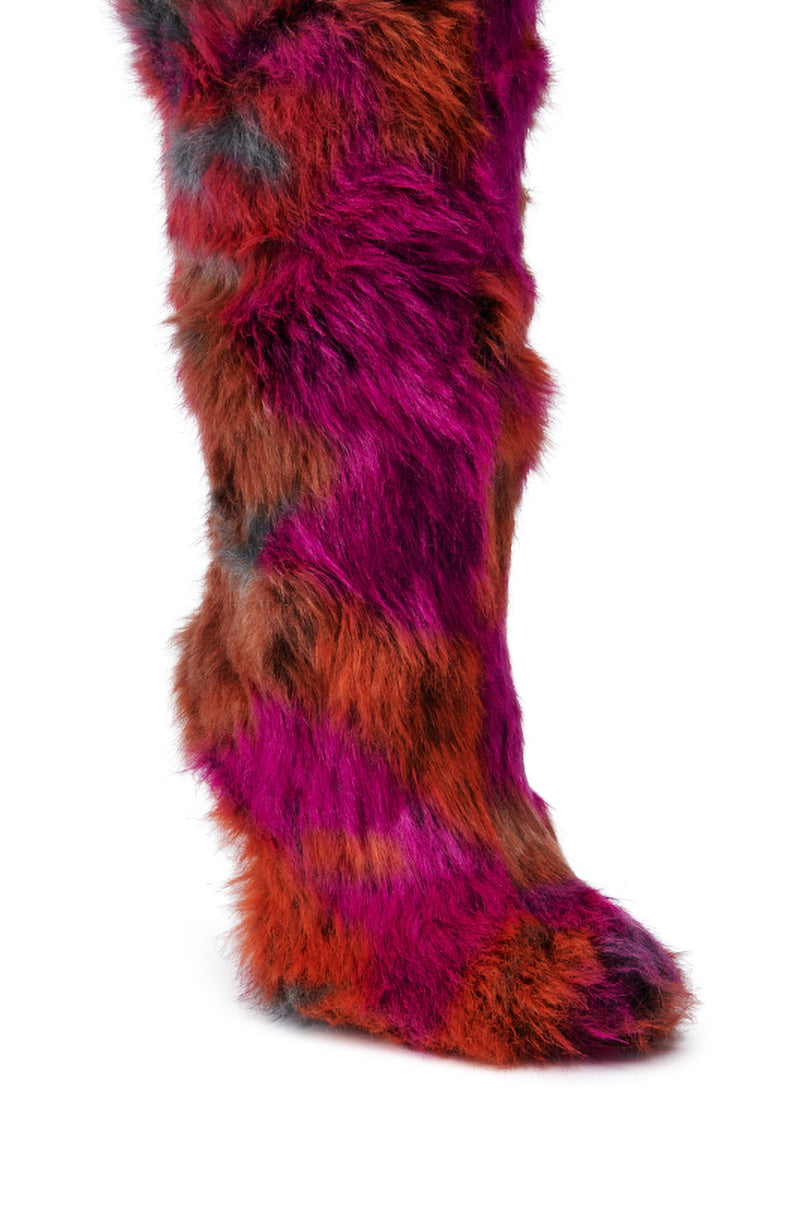 A close-up of the AZALEA WANG UPSETTER ORANGE MULTI FUZZY KNEE HIGH BOOT showcases its fluffy, vibrant faux fur in shades of red and purple. The elegant stiletto heel completes the look, all set against a plain white background.