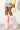 A person wearing the AZALEA WANG UPSETTER PINK STILETTO BOOT, a colorful faux fur knee-high boot in pastel shades of pink, yellow, and blue, holds a small white furry handbag. The outfit features a sheer skirt and a yellow top, set against a light-colored textured wall.